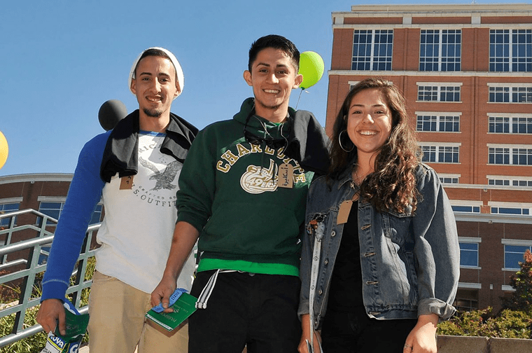 three students smile for the camera during an outdoor event with balloons